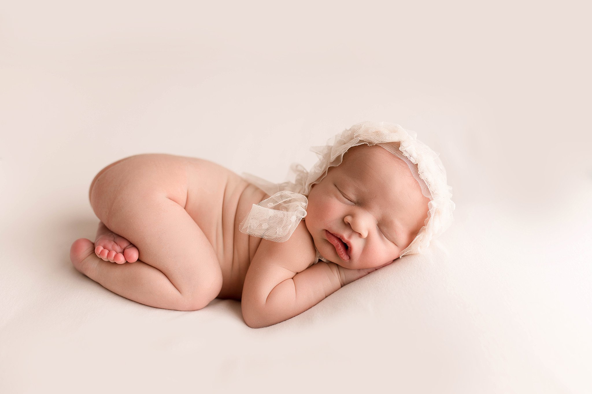 newborn sleeps in a white bonnet in a studio Seattle Midwife