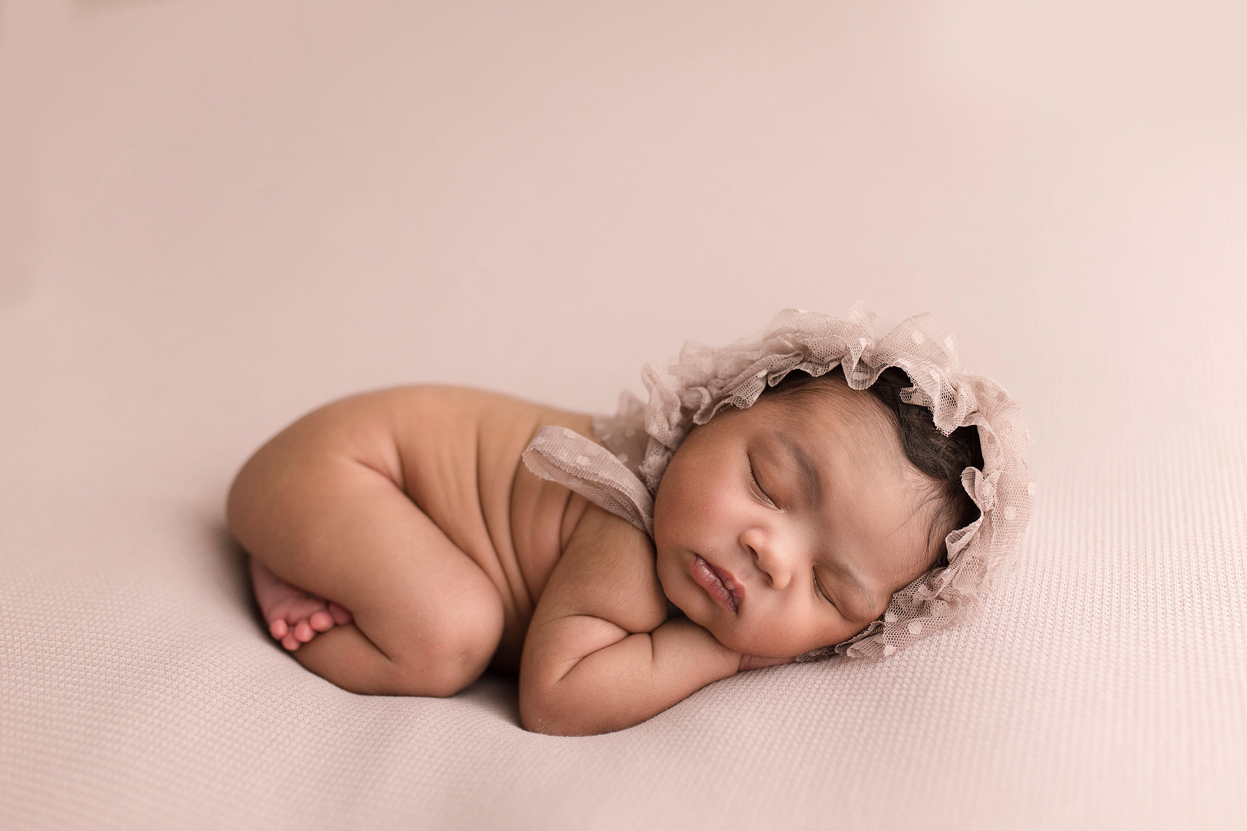 newborn baby sleeps in a tan bonnet on her hands Seattle-Pediatricians