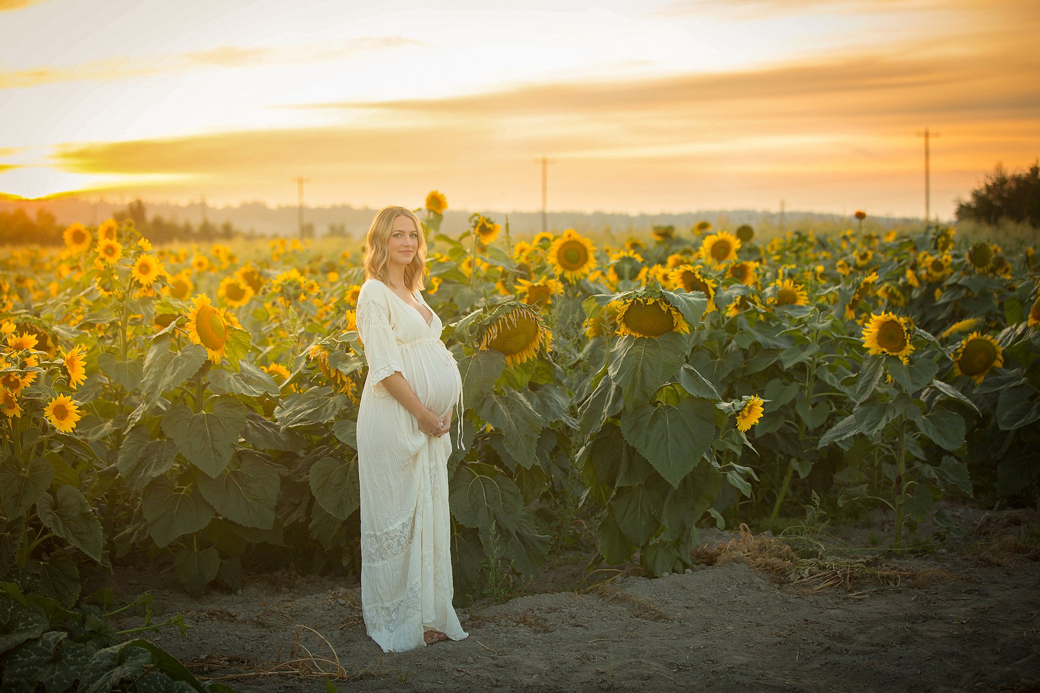 mother to be in a white maternity dress stands in a sunflower field seattle prenatal yoga