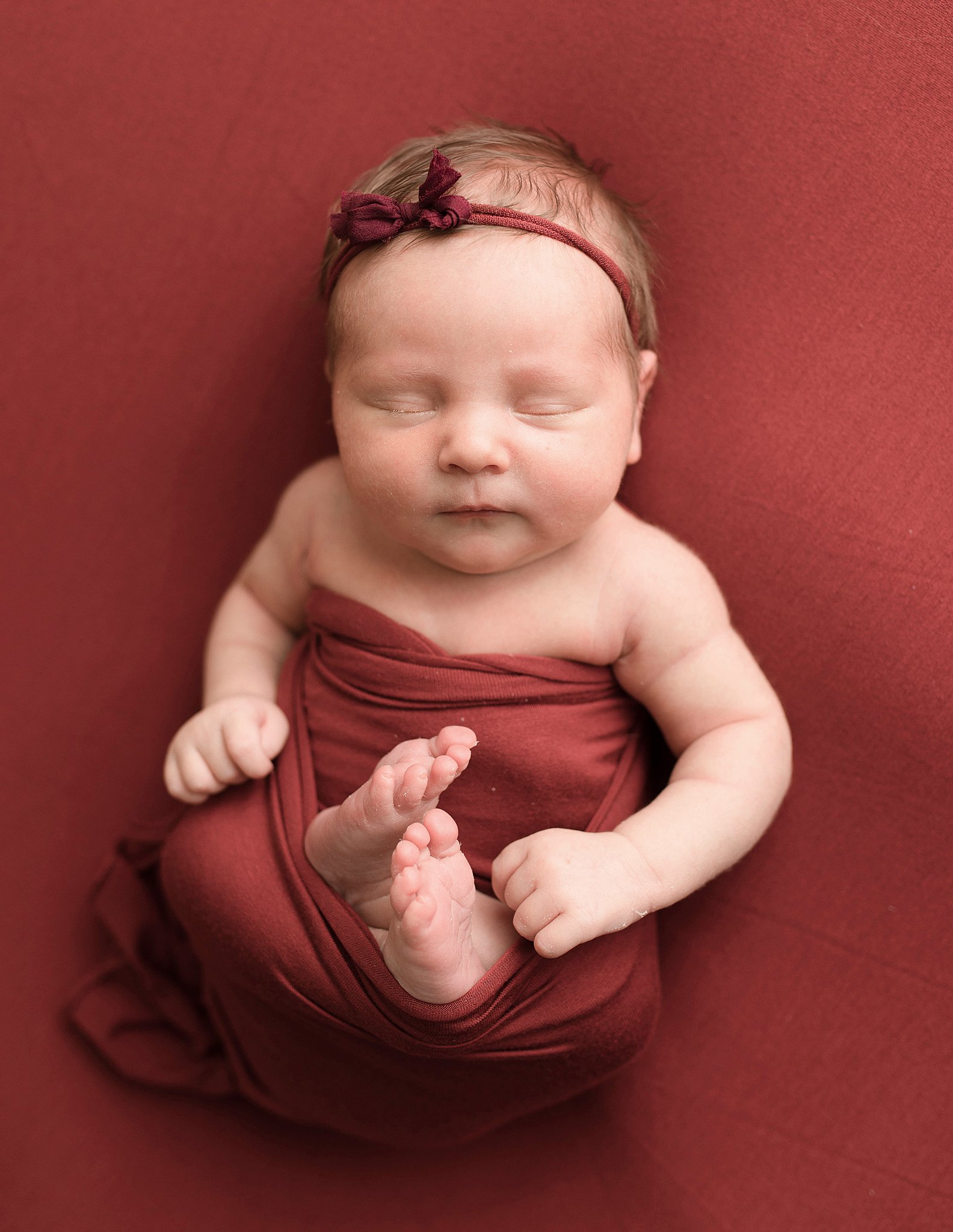 newborn baby sleeps in a red swaddle with arms out on a red bed seattle prenatal yoga